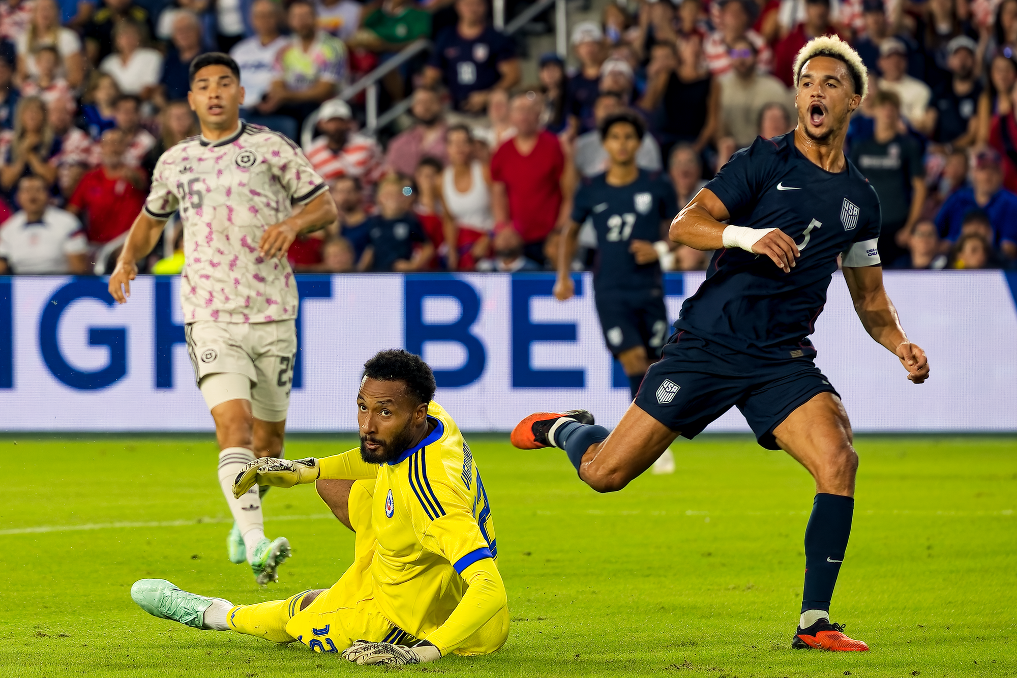 A United States player shouts in frustration after a missed chance as the Chile goalkeeper sits on the grass behind him.
